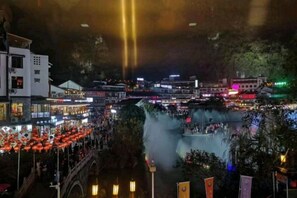 A nighttime view of a riverside area with a bridge, buildings, and a crowd of people. - Shiguangli Homestay (Yangshuo West Street) (Yangshuo)
