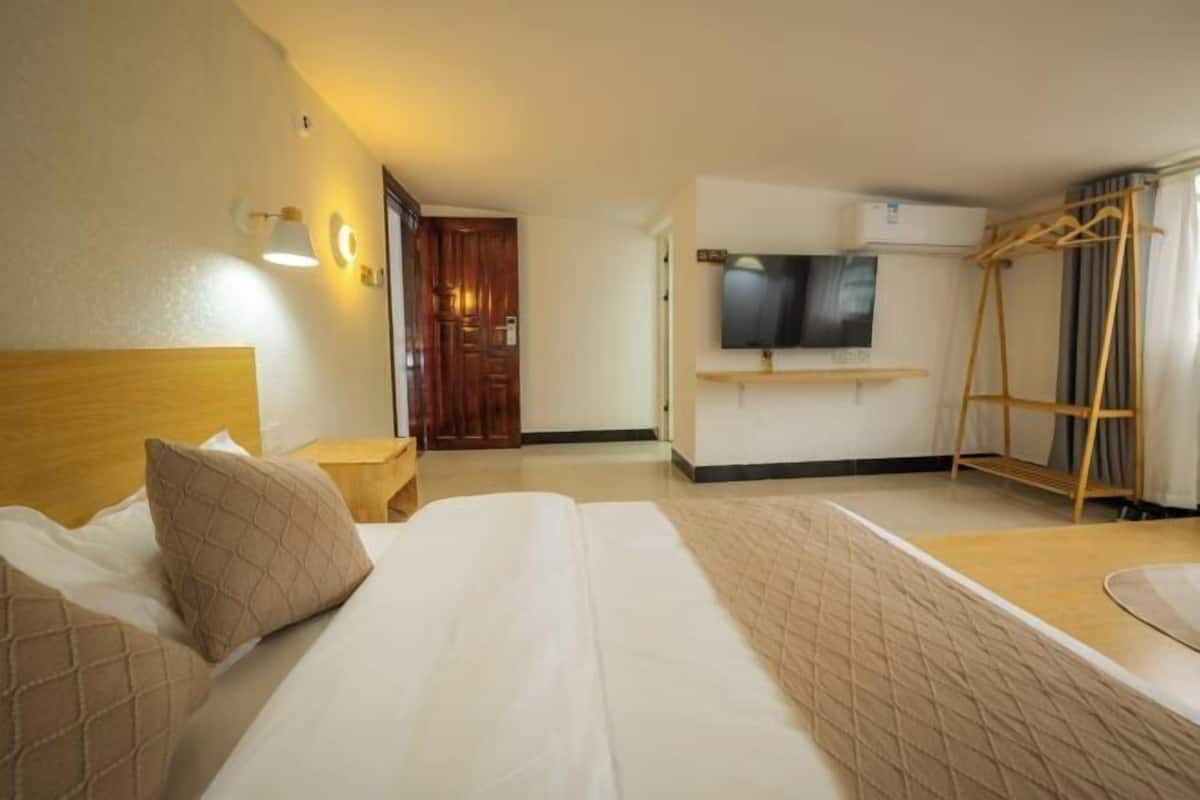 A hotel room with a bed, bedside table, TV, and a wooden wardrobe.