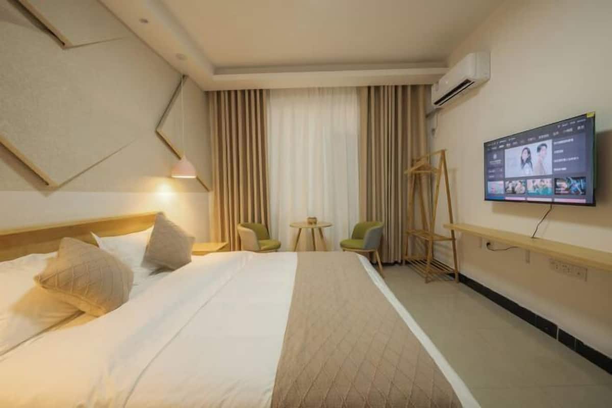 A hotel room with a bed, a TV mounted on the wall, a desk, and a chair.
