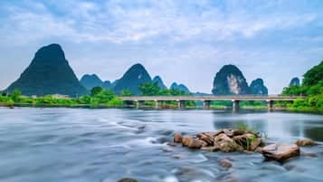 A river with a bridge, rocky foreground, and mountains in the background.