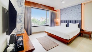 Ein Hotelzimmer mit einem großen Bett, einem Flachbildfernseher, einem Holztisch, einer Kaffeemaschine und Blick auf die Stadt durch das Fenster.
