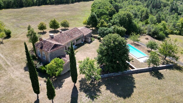 An aerial view of a property with a large house, a swimming pool, and surrounding greenery.