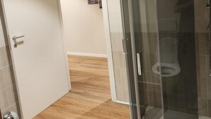 Ett modernt badrum med en duschkabin i glas, en toalett och ett trägolv.
