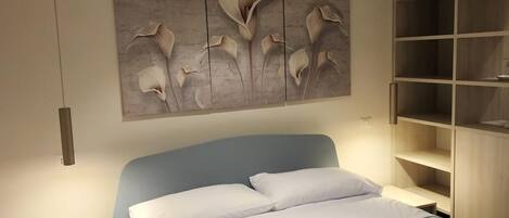 Un dormitorio moderno con cama, mesita de noche, estante en la pared y un adorno mural.