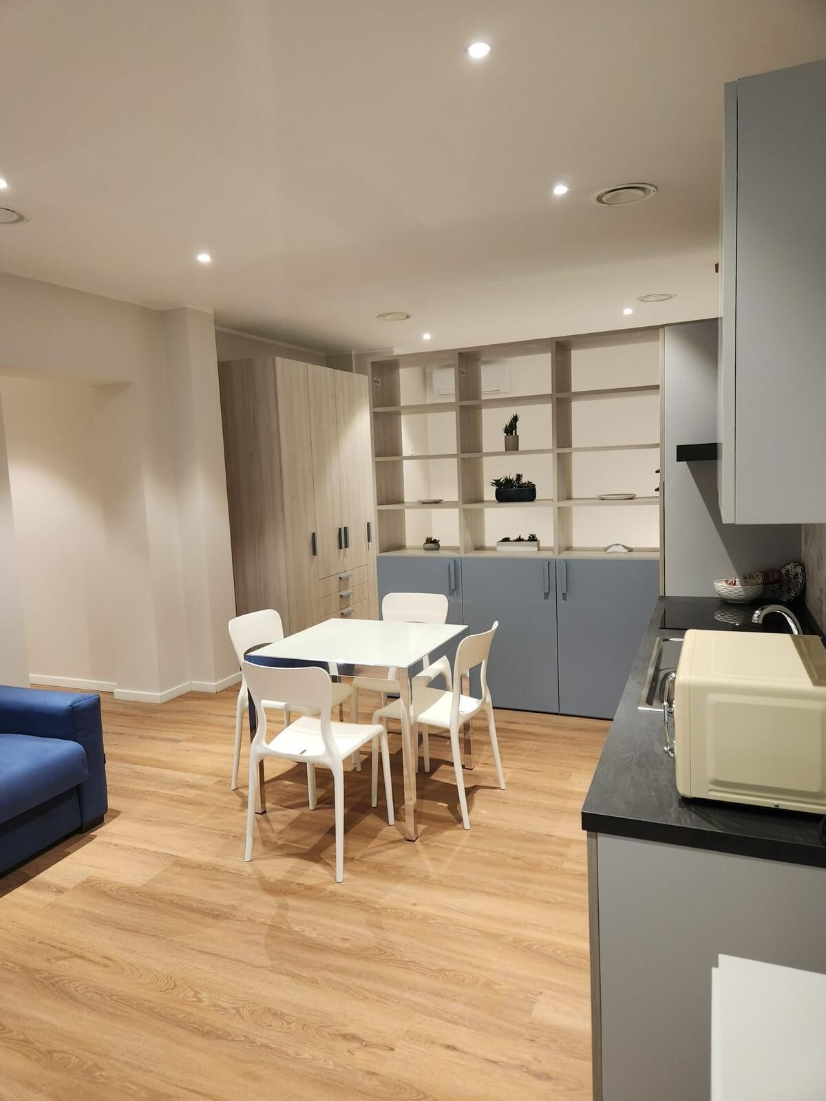 Una cocina moderna con armarios blancos, una mesa de comedor con sillas y un sofá azul.