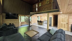 Amplia sala de estar con un sofá moderno, una pequeña mesa de centro de madera y una escalera en espiral que lleva a un nivel superior.