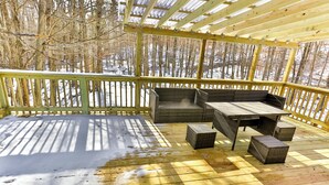 Una terraza de madera con pérgola, mobiliario de mimbre y vistas a un bosque nevado.
