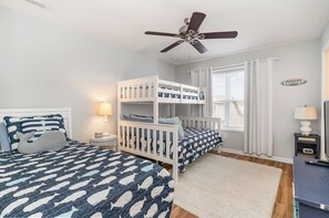 A bedroom with two bunk beds, a ceiling fan, a window with curtains, and a welcome sign.