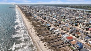 A coastal residential area with houses along the beach, a pier extending into the water, and a road parallel to the shore.