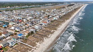 Un quartier résidentiel situé sur la côte, avec des maisons le long de la plage, une jetée et une vue sur l’océan.