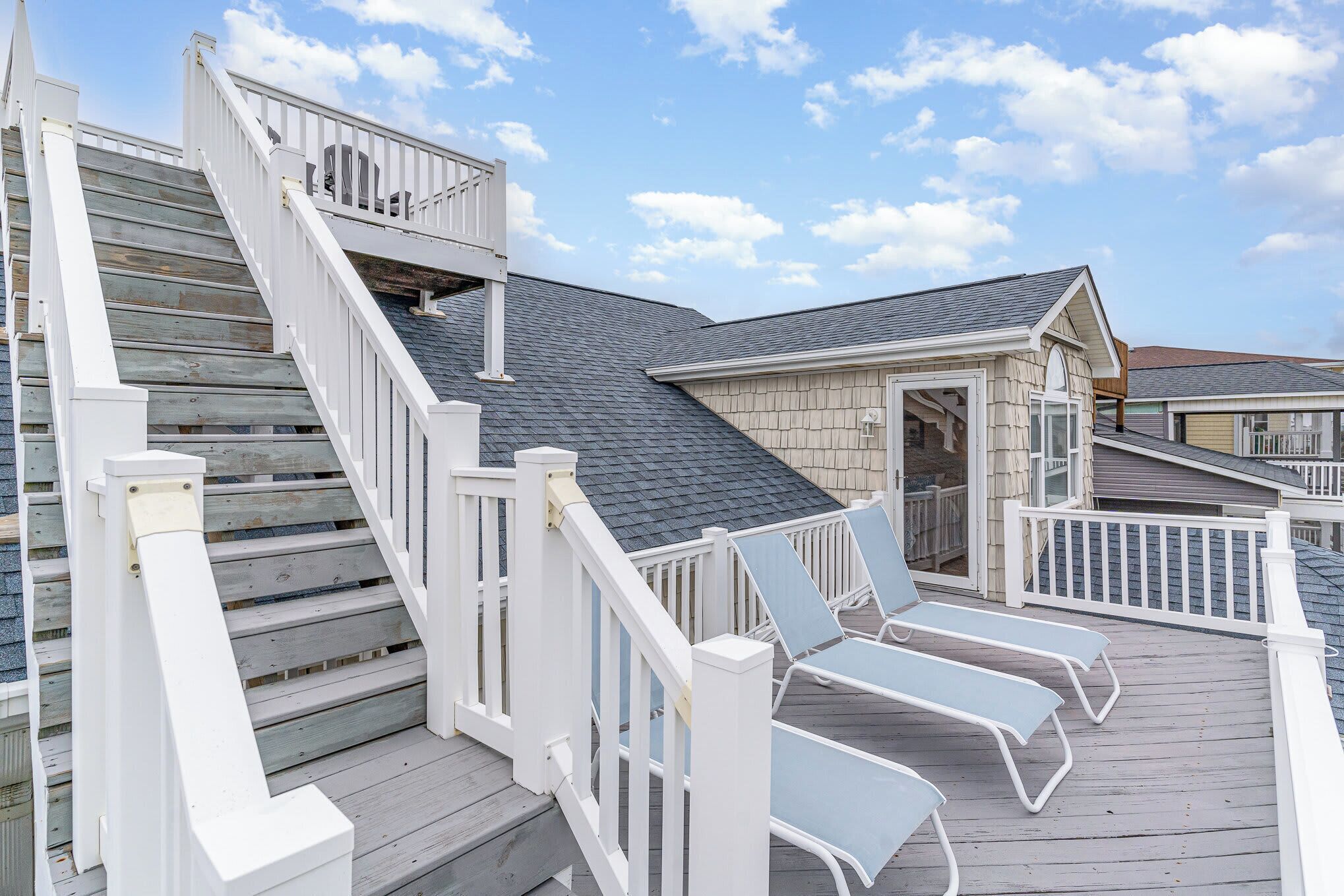 A wooden deck with white railings, a set of stairs, and two lounge chairs.