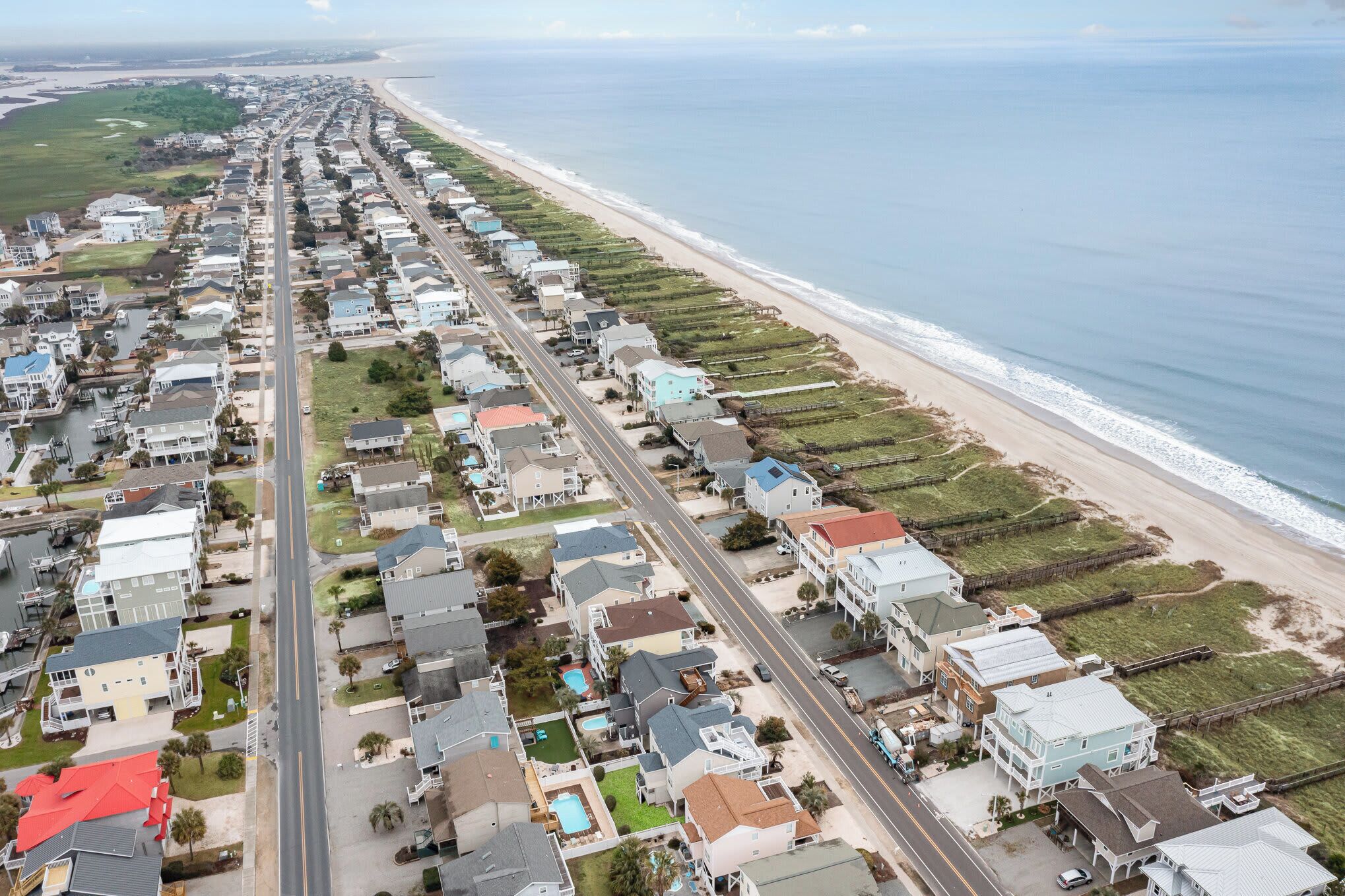 Vista aerea di una zona residenziale costiera con case disposte lungo una strada che conduce alla spiaggia.