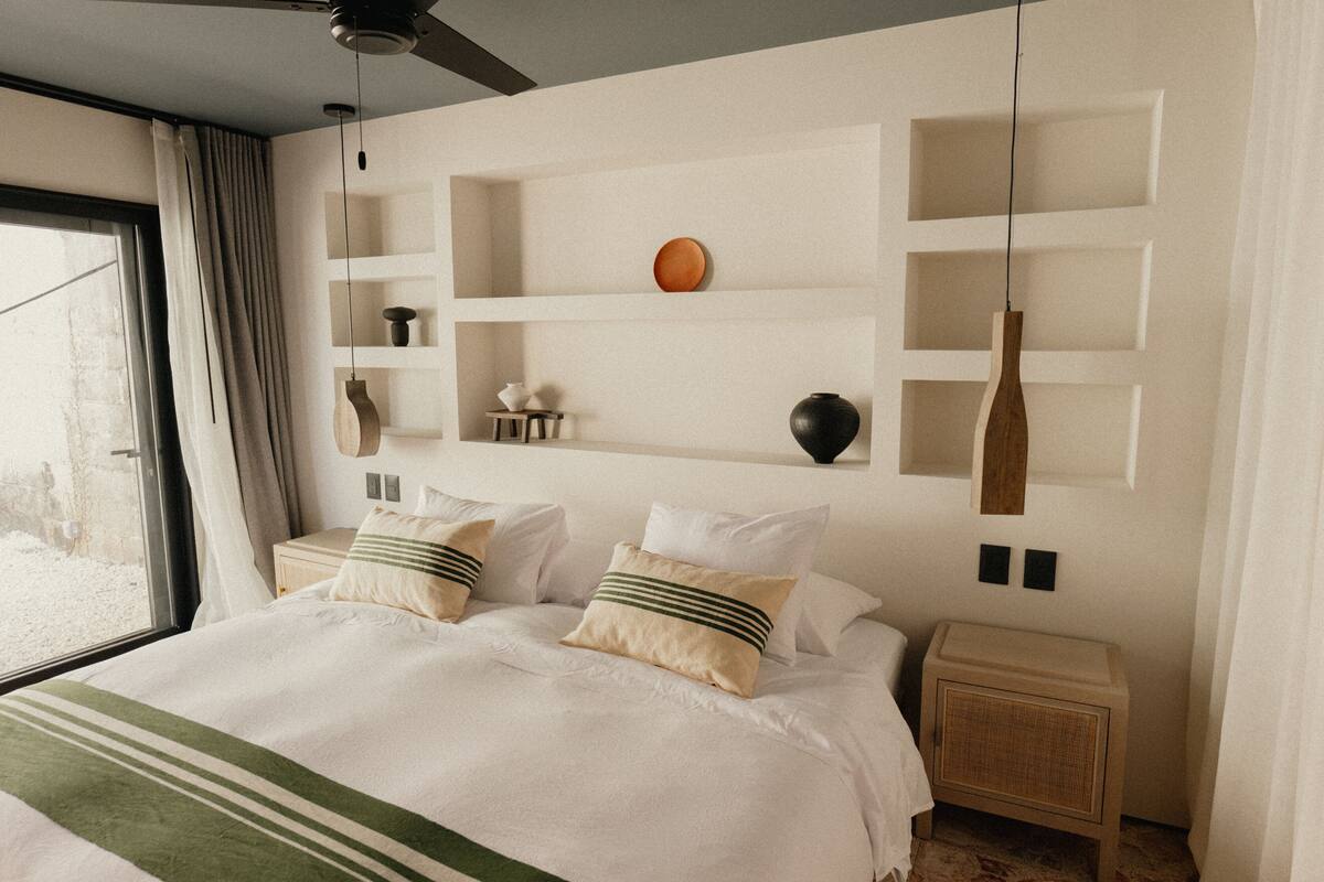 Ein ordentlich eingerichtetes Schlafzimmer mit einem großen Bett, Nachttischen und einem an der Wand befestigten Regal mit dekorativen Gegenständen.