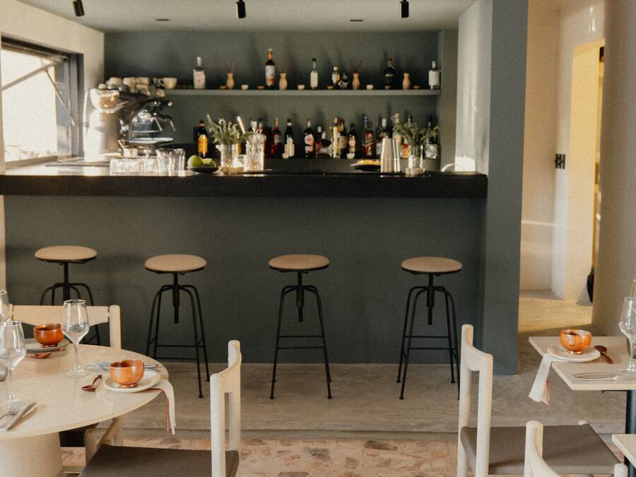 Una zona de bar con taburetes y una barra repleta de botellas.
