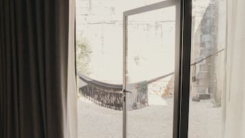 Una habitación con un amplio ventanal corredero que da a un espacio exterior con grava y una hamaca.