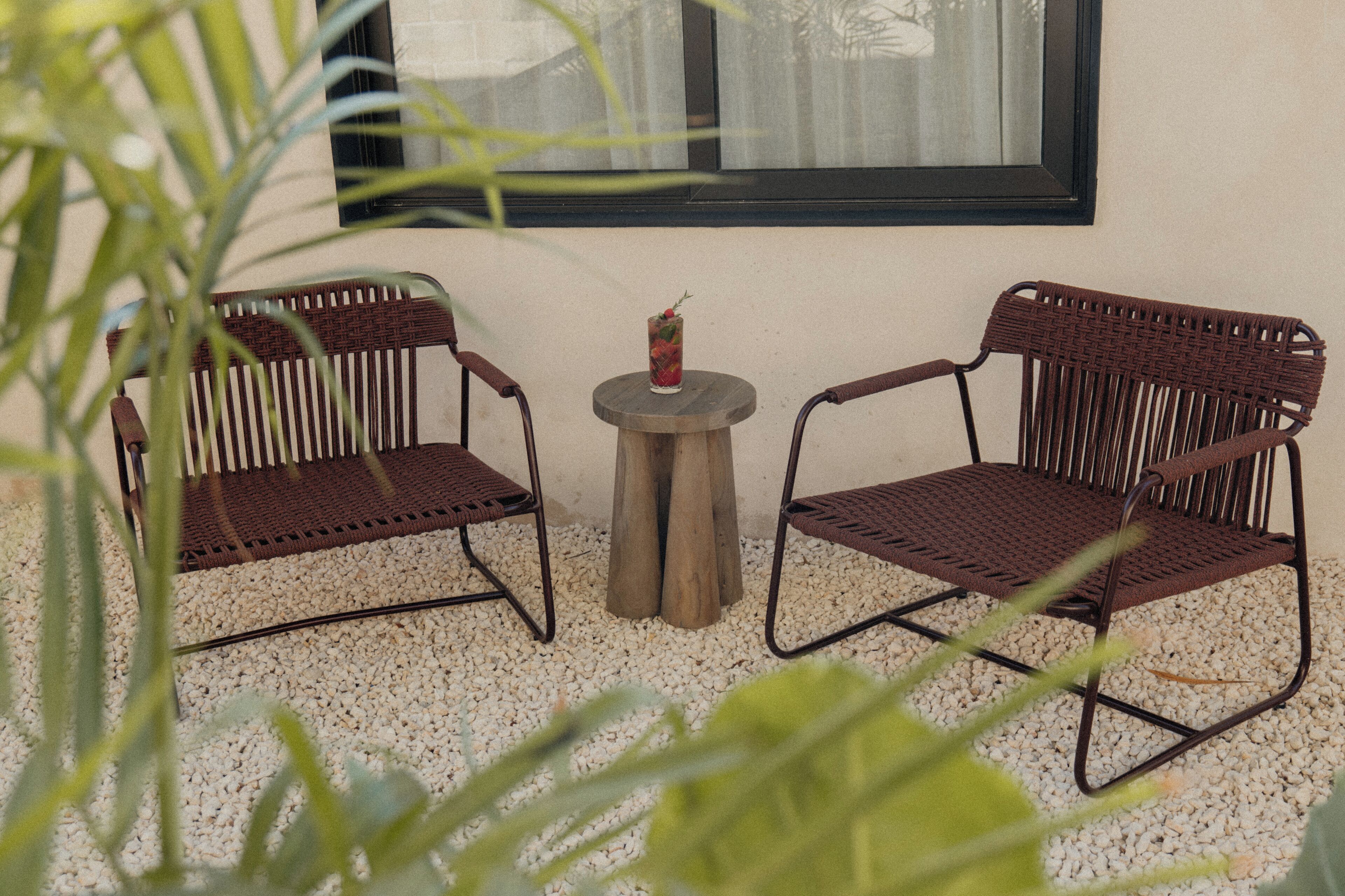 Twee rieten stoelen met metalen frames, een klein houten tafeltje en een glas met een drankje.