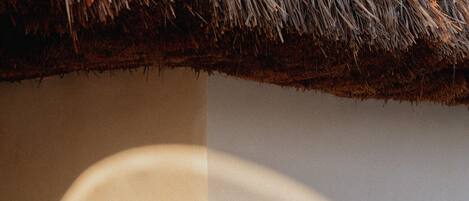 A shadow of a hand on a wall with a thatched roof.