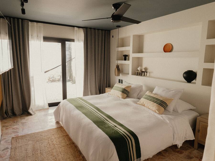 A bedroom with a large bed, a ceiling fan, and a view of the outdoors.