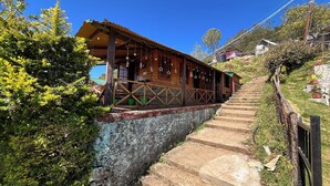 A wooden building with a porch, stone steps, and a view of a hillside. - Mount Olympus Hood cabin (Kodaikanal)