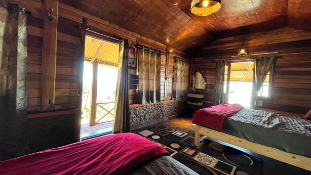 A wooden cabin room with two beds, a stone wall, and a window with curtains. - Mount Olympus Hood cabin (Kodaikanal)