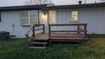 En træterrasse med trapper op til et hus med hvid facade og sort tag.