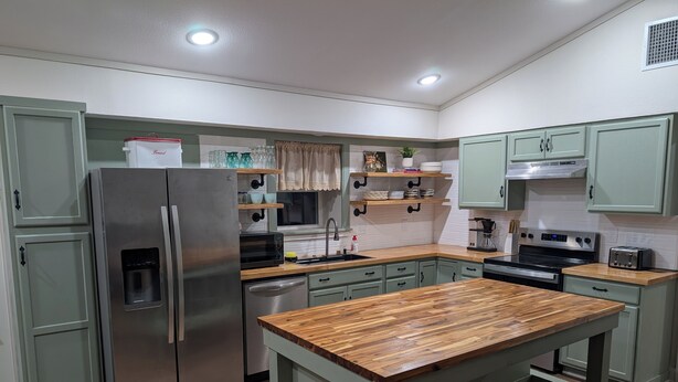 Eine moderne Küche mit grünen Schränken, Edelstahlgeräten und einer Holztheke.