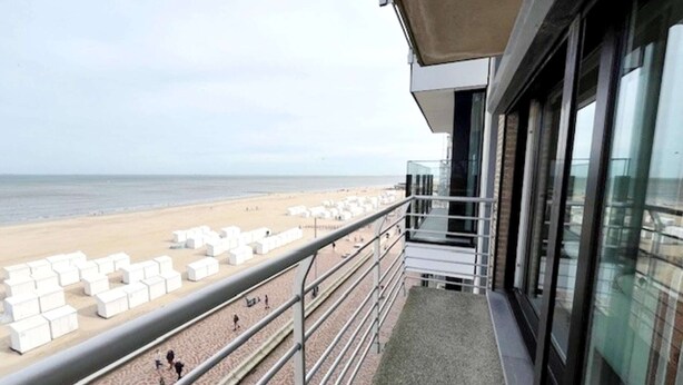 Un balcon donnant sur la plage, avec des chaises longues blanches et une rambarde en métal.