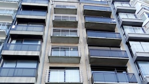Un immeuble résidentiel à plusieurs étages, doté de balcons, de grandes fenêtres et d’une façade en briques.