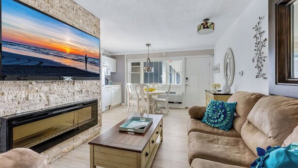 Una sala de estar con chimenea, un televisor montado en una pared de piedra, un sofá color beige y una zona de comedor al fondo.
