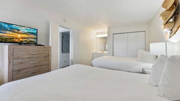 Ein Hotelzimmer mit einem großen Bett, einer Holzkommode, einem Fernseher, der einen Sonnenuntergang zeigt, und einem an der Wand befestigten Hutfänger.