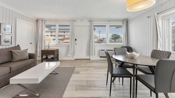 A modern living room with a sofa, coffee table, dining table with chairs, and a pendant light. - Beachcomber Resort 1bedroom Queen suite (Avalon)