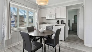 A modern kitchen with white cabinetry, a central island, and a dining area with a round table and chairs. - Beachcomber Resort 1bedroom Queen suite (Avalon)