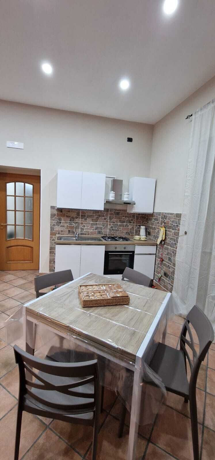 Una cucina compatta con mobili bianchi, una parete di fondo in pietra e un pavimento piastrellato.