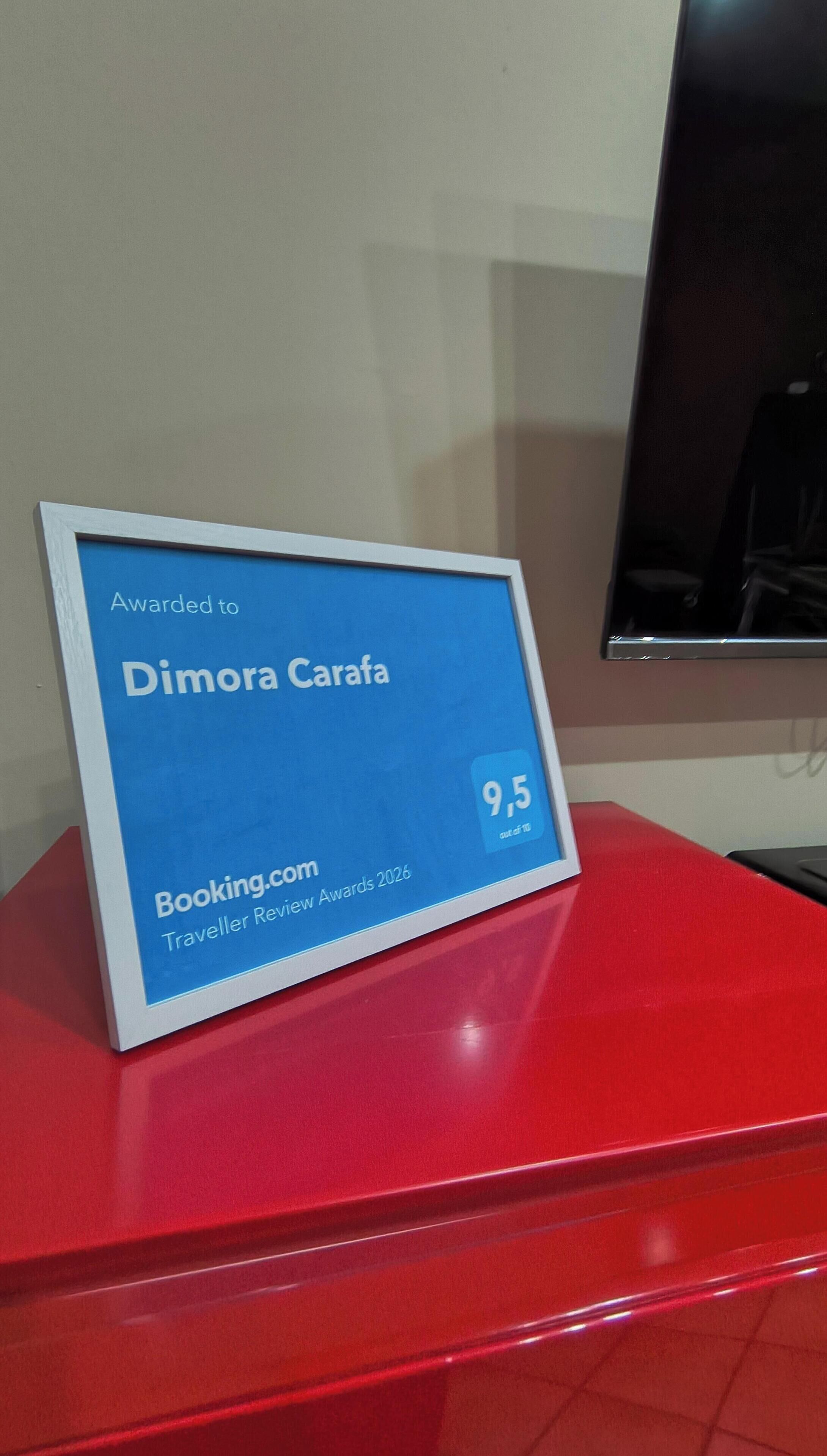 A blue award plaque on a red surface, stating "Awarded to Dimora Carafa" and "Booking.com Traveller Review Awards 2020".