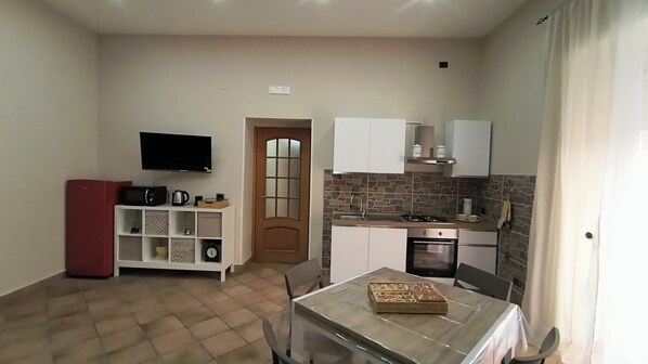 A compact kitchen with a TV, a refrigerator, a dining table, and a stone backsplash.