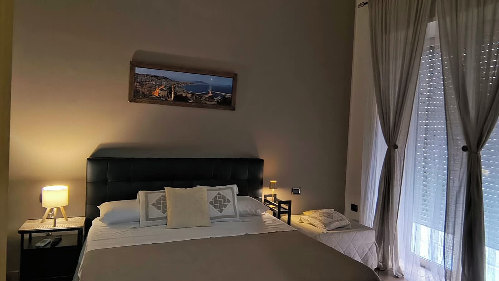 Une chambre d’hôtel avec un grand lit, deux tables de chevet, une commode, un tableau au mur et une fenêtre avec des rideaux.