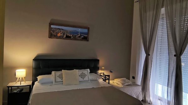 Habitación de hotel con una cama grande, dos mesitas de noche, una lámpara de noche, un cuadro en la pared y una ventana con cortinas.