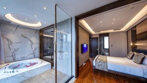 Un dormitorio moderno con una cama grande, cabina de ducha con mampara de vidrio y baño con suelo de mármol.