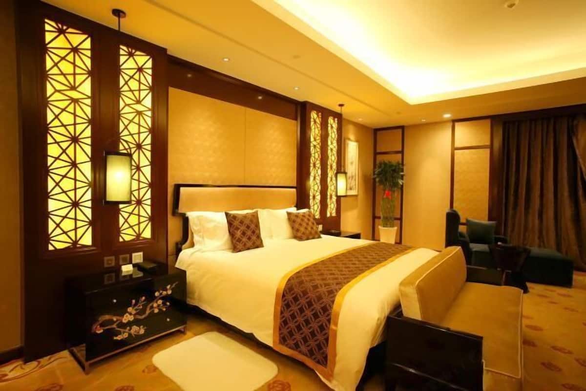 Een hotelkamer met een groot bed, nachtkastjes, een bureau, een stoel en een potplant.