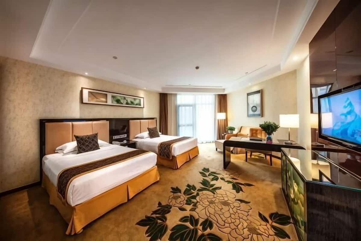 Een hotelkamer met twee bedden, een bureau, een televisie en een groot raam.
