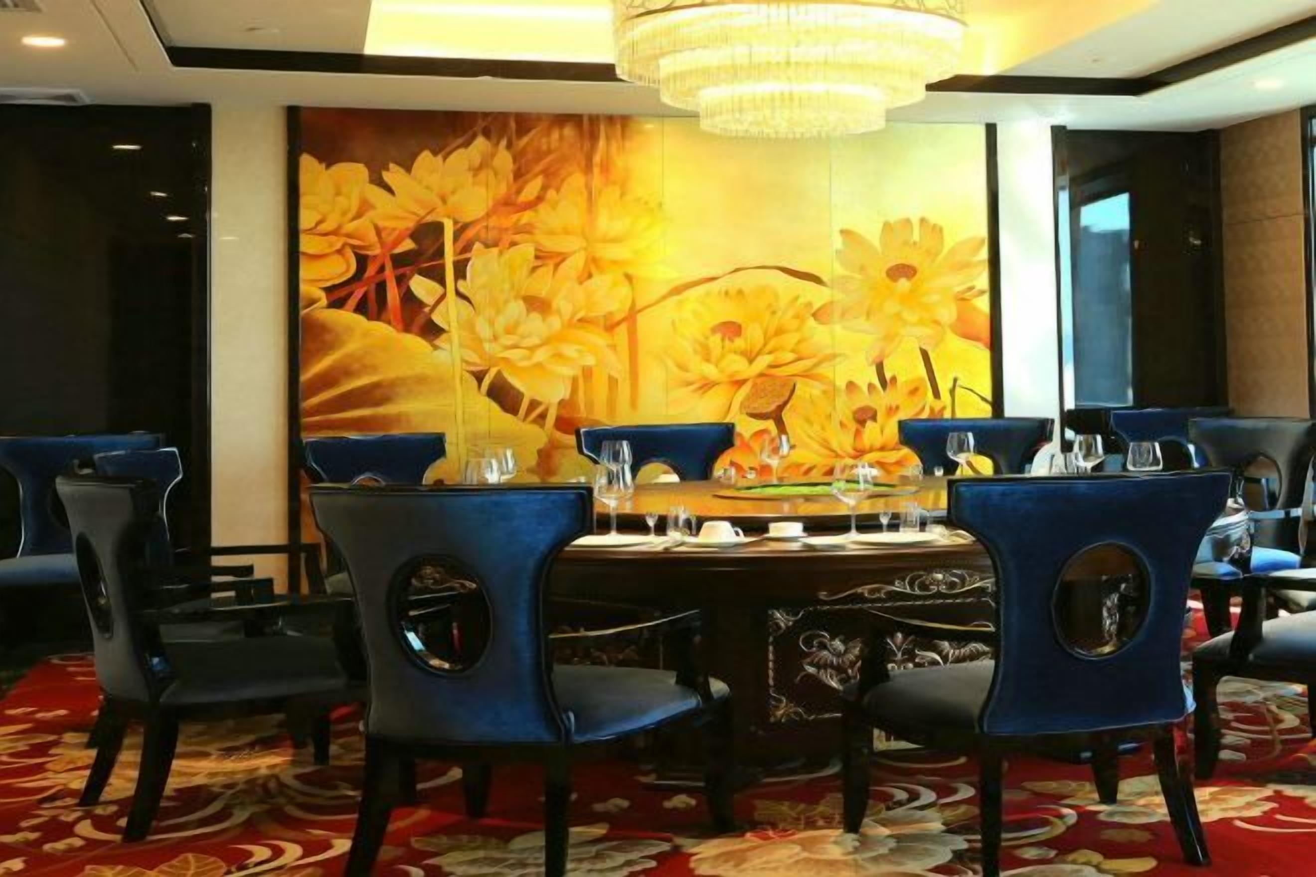 A dining area with a round table, blue chairs, and a large floral mural on the wall.
