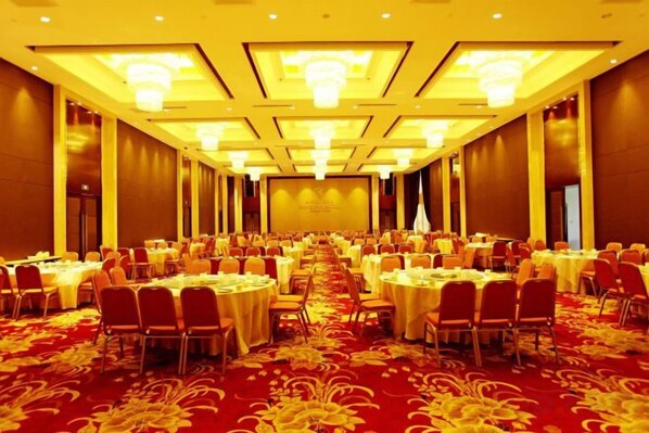 A banquet hall with round tables and chairs, a red carpet, and a stage at the front.