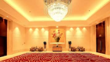 A spacious room with a patterned carpet, a chandelier, and a reception desk with chairs.