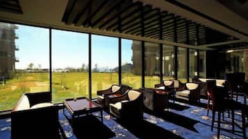 Een moderne hotelkamer met grote ramen, uitzicht op een golfbaan en een zithoek met banken en een tafel.