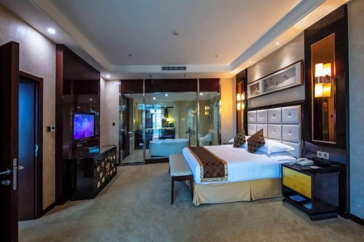 Een hotelkamer met een bed, nachtkastje, televisie en een glazen scheiding naar een badkamer.