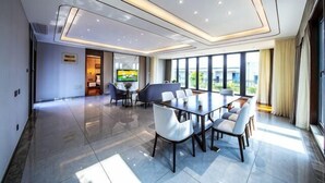 Una habitación de hotel moderna con un amplio comedor, asientos cómodos, un televisor de pantalla plana y ventanas grandes que ofrecen vistas al exterior.