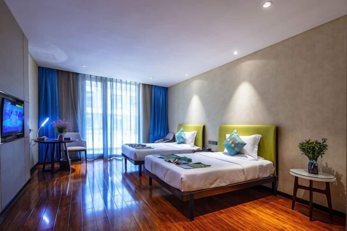 Een hotelkamer met twee bedden, een bureau, een televisie en een raam met gordijnen.