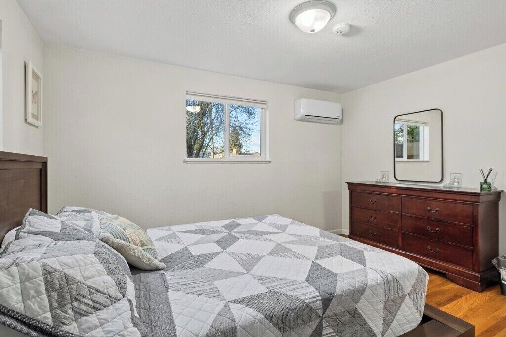 Ein Schlafzimmer mit Bett, Kommode, Fenster und Klimaanlage.