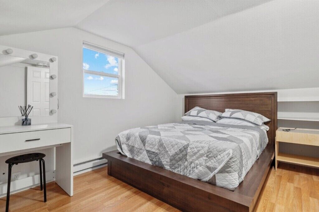A bedroom with a bed, a desk, a chair, a vanity with a mirror, and a window.