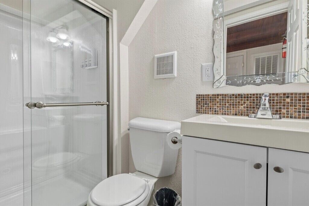 Bany amb porta de vidre per a la dutxa, un vàter, un lavabo amb resclosa de rajola i un mirall amb marc decoratiu.